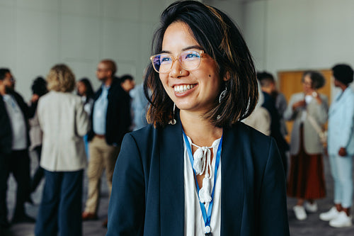 Smiling businesswoman wearing glasses at a networking conference with colleagues in the background