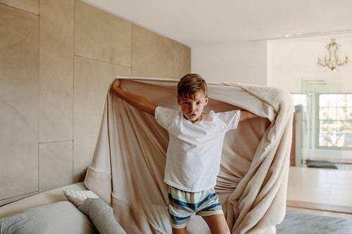 Cute little boy standing on bed with a blanket