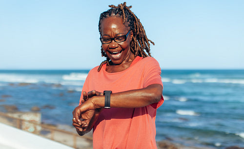 Joyful senior African American woman checking time on beach