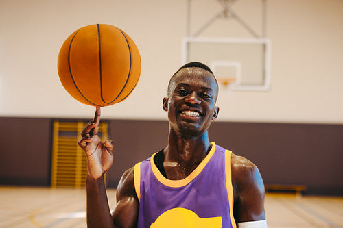 Basketball player spinning ball on finger with joyful expression on court