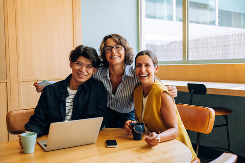 Three colleagues smiling in an office setting with relaxed and happy expressions