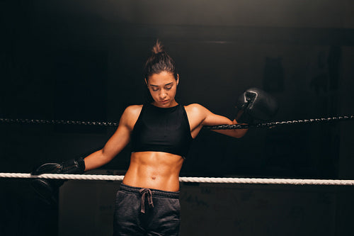 Athletic young woman leaning against the ropes in a boxing ring