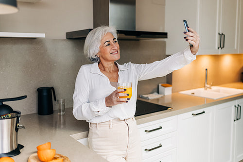 Cheerful senior woman taking a video call in her kitchen at home