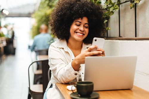 Woman with Afro hair sits in a cafe, reading a text message on her smartphone