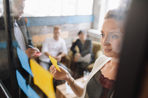 Creative business woman sticking adhesive notes on glass wall