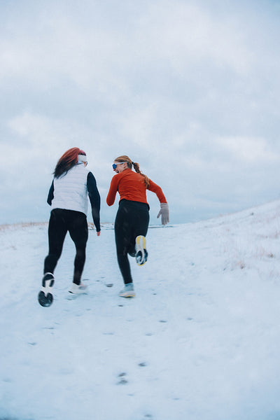 Women race playfully to the hilltop in snowy winter running session