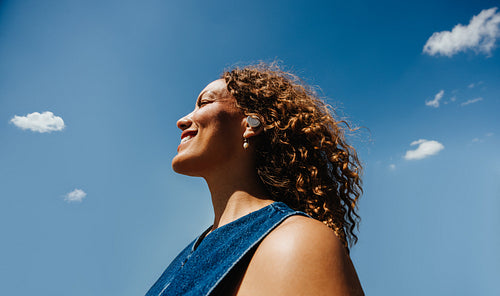 Curly-haired woman enjoys music outdoors under blue sky