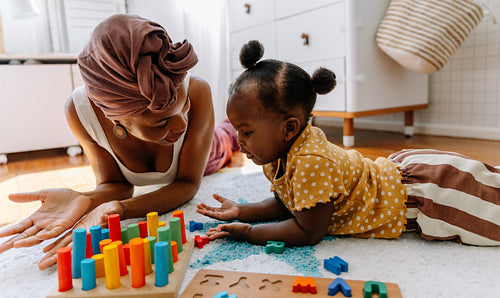 Mother teaching toddler through play with colorful blocks at home
