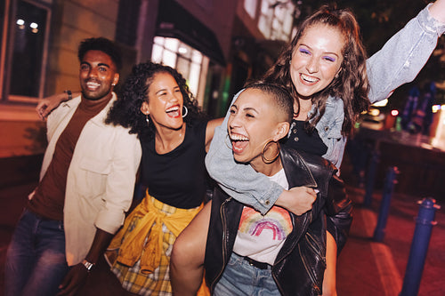 Blissful young woman piggybacking her friend outdoors at night