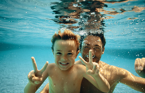 Father and son posing underwater with peace signs