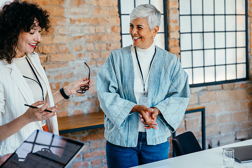 Accomplished businesswomen engaging in a friendly team meeting in a modern office with exposed brick walls, showcasing confidence and teamwork