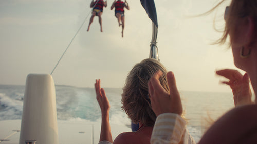 People cheering as friends parasail across the open ocean during golden hour