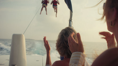 People cheering as friends parasail across the open ocean during golden hour