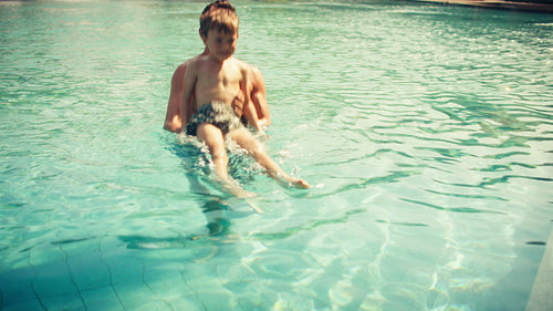 Father and child playing happily in the clear swimming pool, splashing and laughing on a sunny day