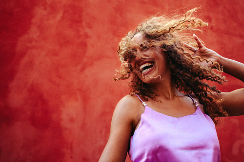 Woman smiles with curly hair in motion outdoors by a red wall