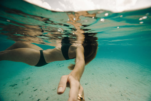 Woman swimming underwater reaching out in clear blue tropical water