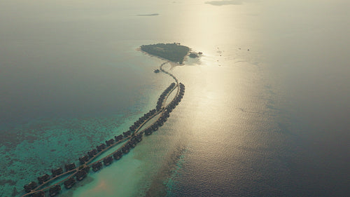 An aerial drone view showcases a luxurious island resort with overwater bungalows in a tropical ocean