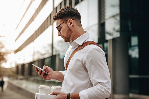 Businessman checking mobile phone standing on street