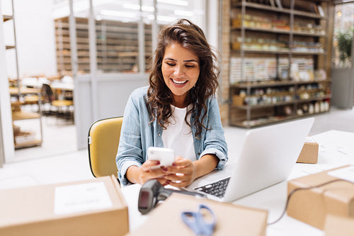 Cheerful online store owner reading a text message on her smartphone