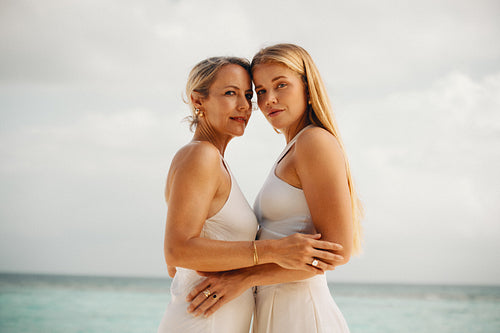Elegant women showcasing white dresses and gold jewelry by the seaside