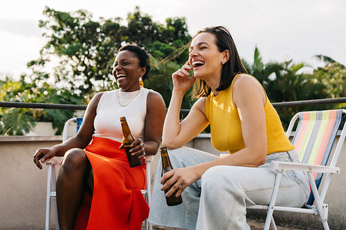 Friends sitting on rooftop, relaxing with beers and laughter