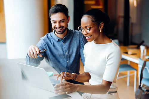 Two professionals at a desk using a laptop in a bright office setting