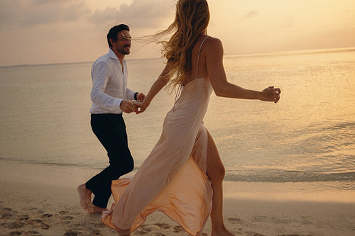 Happy couple chasing each other on the beach at sunset, enjoying time together