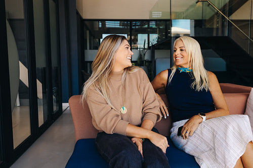 Two women sitting on a couch and smiling in a modern office setting