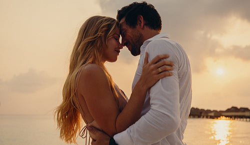 Loving embrace between husband and wife at sunset on tropical island beach