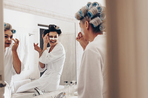 Happy mother and daughter applying face cream standing in the bathroom