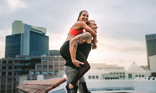 Female athlete piggy riding on a man while training on rooftop