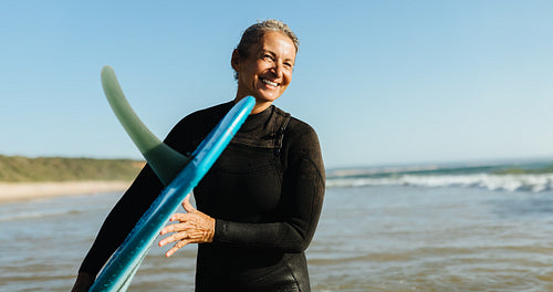 Mature woman with a single fin surfboard at the beach