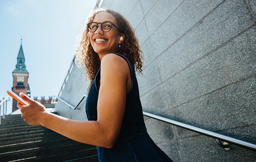 Commuting woman checks smartphone while ascending sunny city stairs