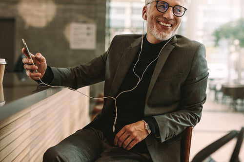 Businessman at cafe listening music from smart phone