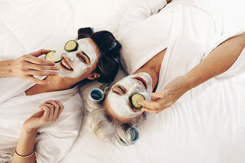 Top view of smiling mother and daughter lying on bed with face pack