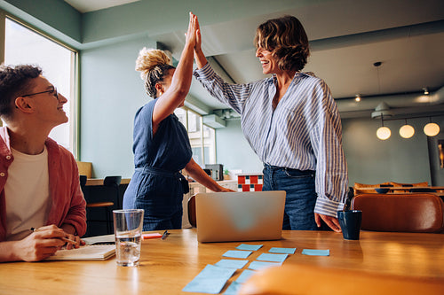 Group of colleagues celebrating success with high-five in meeting environment