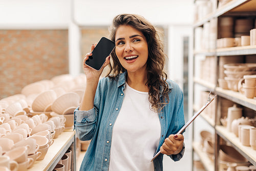 Contemplative ceramist holding a smartphone in her shop