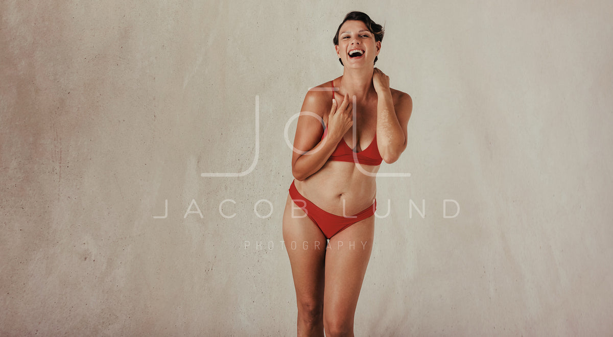 Mature woman embracing her natural and aging body. Confident woman wearing black  underwear and smiling cheerfully while standing alone against a studio  background. stock photo