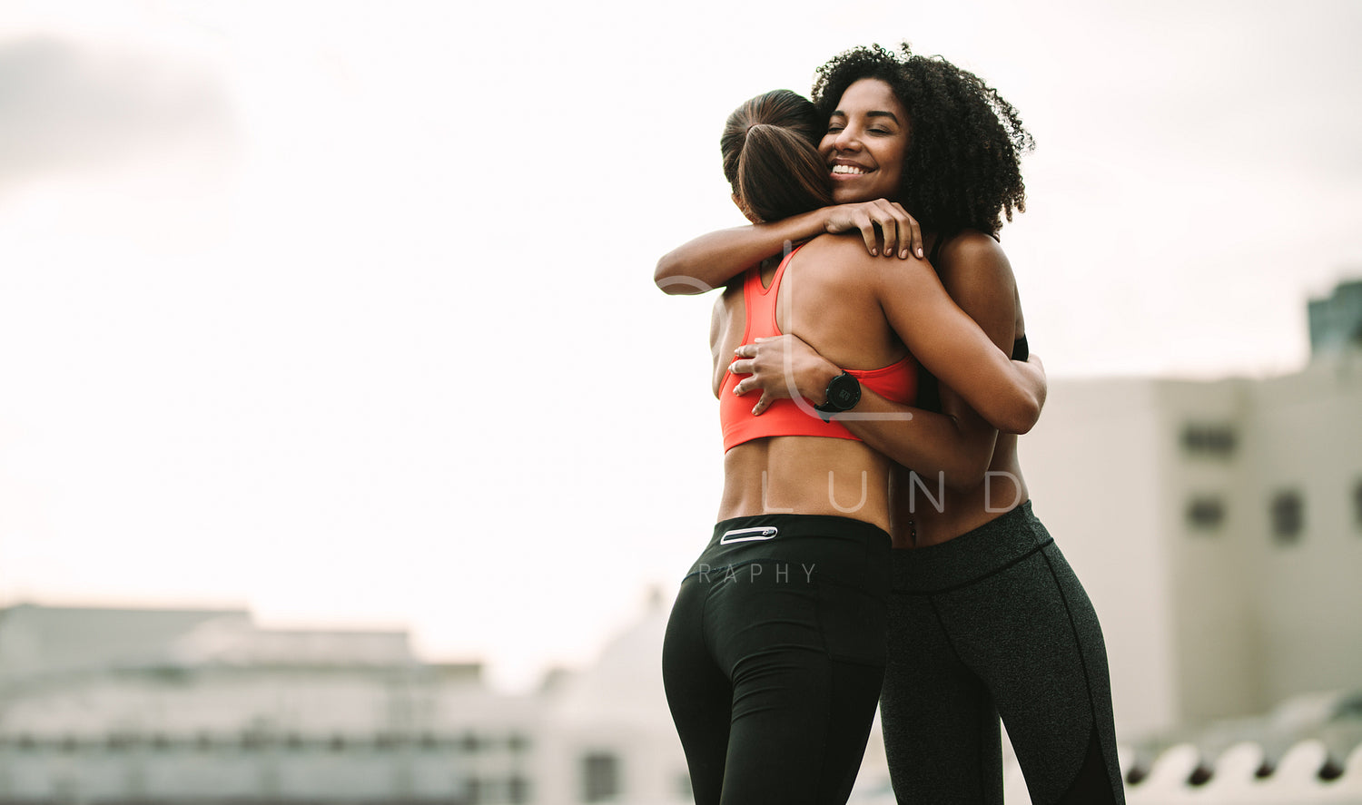 Two women in fitness wear hugging each other standing on rooftop