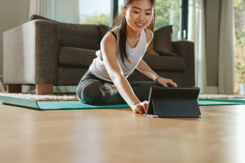 Happy young chinese woman sitting yoga pose and watching instructional  videos on digital tablet. Fit woman watching fitness tutorial on tablet  computer at home and doing yoga workout. stock photo