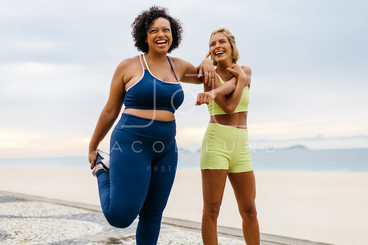 Two happy women doing warm-up exercises on the beach – Jacob Lund  Photography Store- premium stock photo