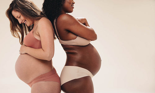 Two pregnant women wearing underwear in a studio, showing their
