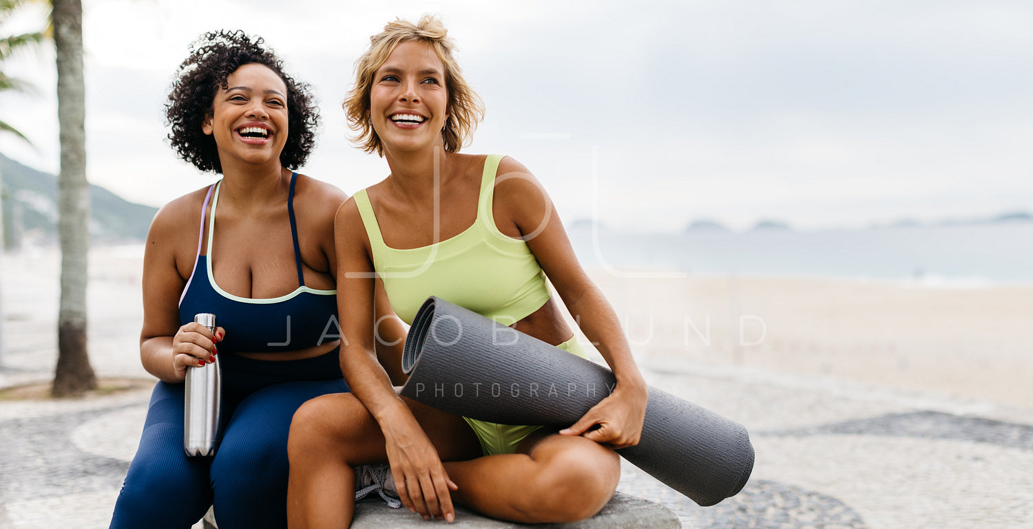 Two happy women sitting on the promenade with beach workout