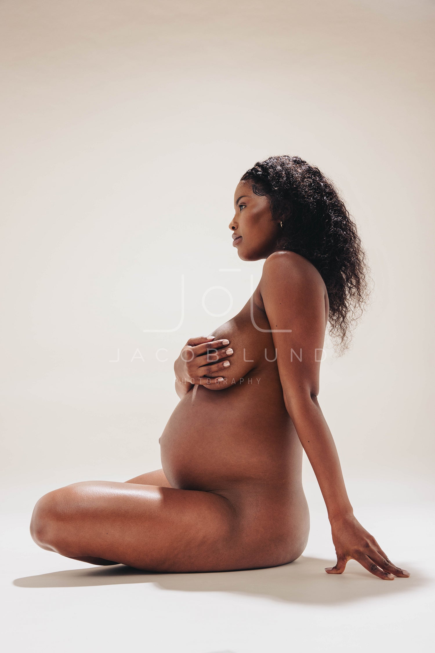 Naked, dark-skinned pregnant woman embracing her maternity body in