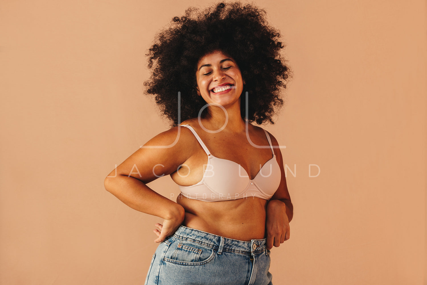 Curvy woman smiling happily while wearing a bra and jeans – Jacob