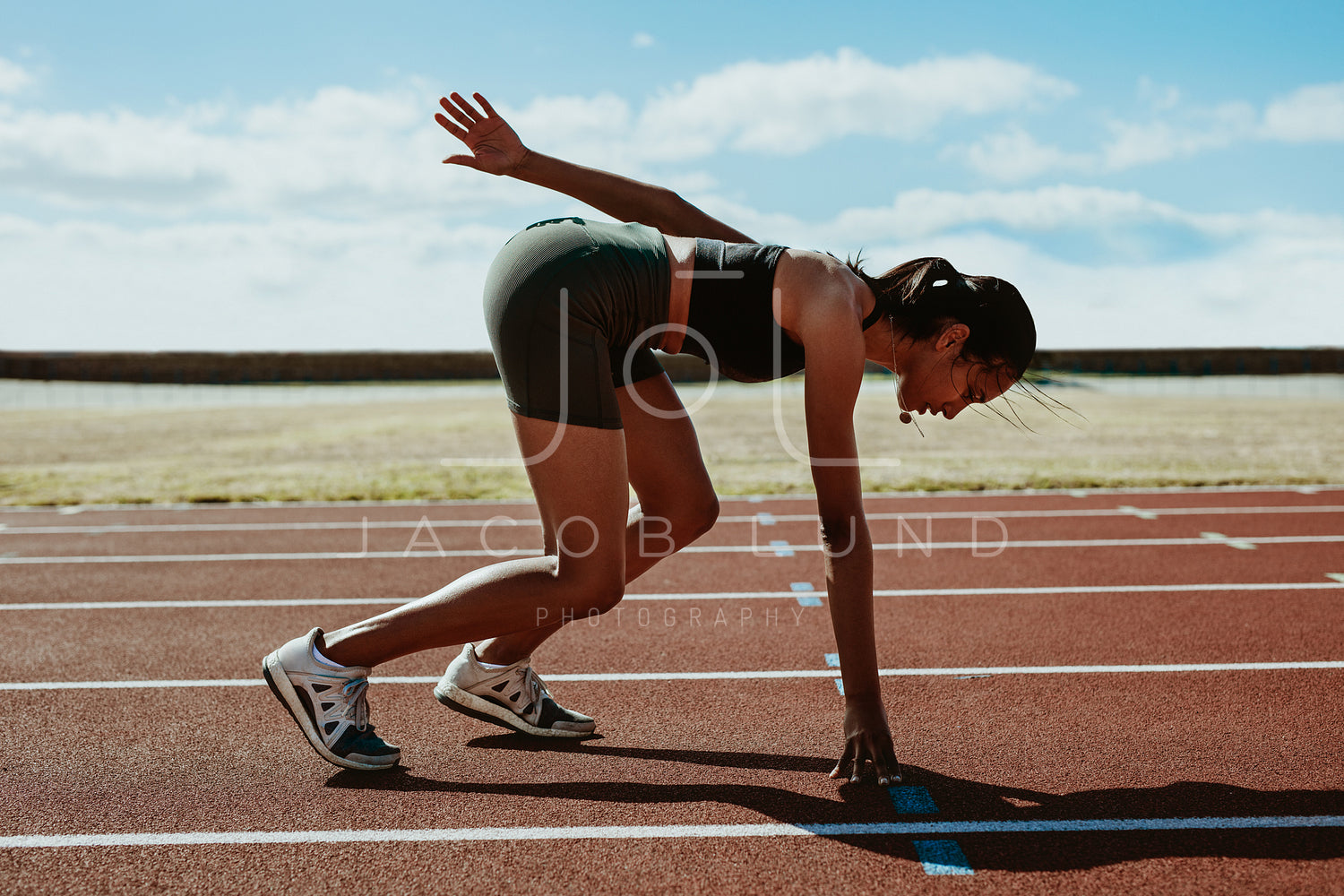 Female athlete taking position on her marks to start off the run. Side view  of female runner sitting at the start line on running track on a black  background. stock photo