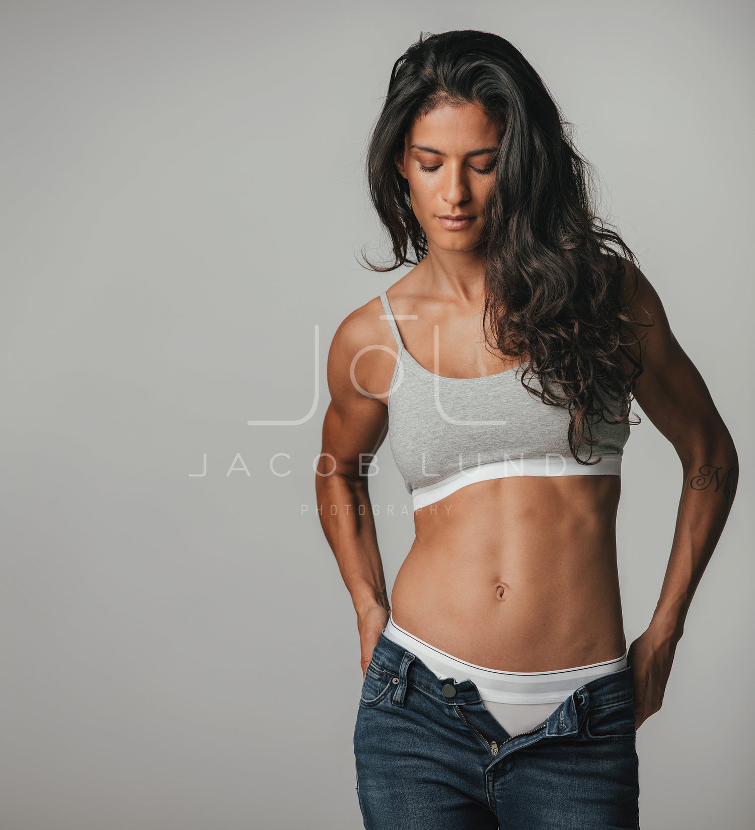 Fit young woman in unbuttoned tight blue jeans and gray sports bra