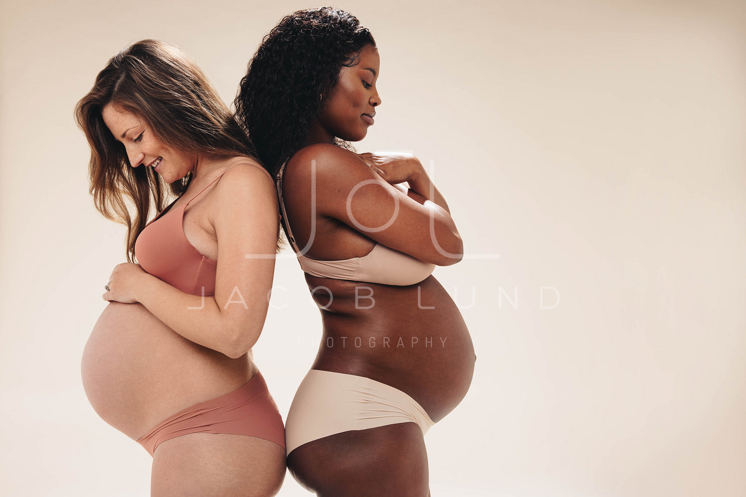 Two pregnant women wearing underwear in a studio, showing their