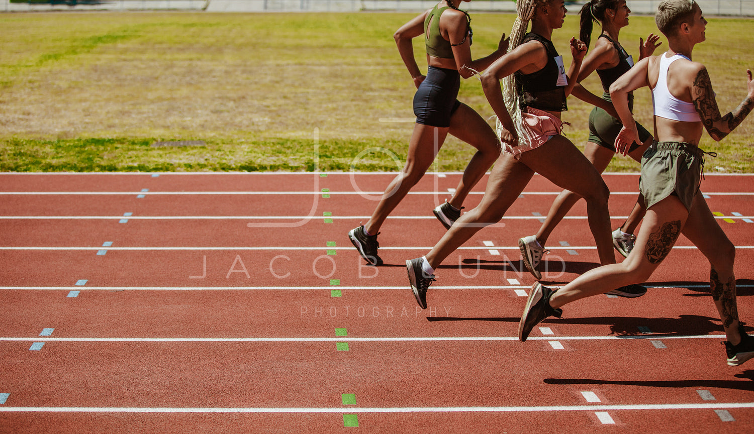 Female athletes running in competition on blue track - Stock Image