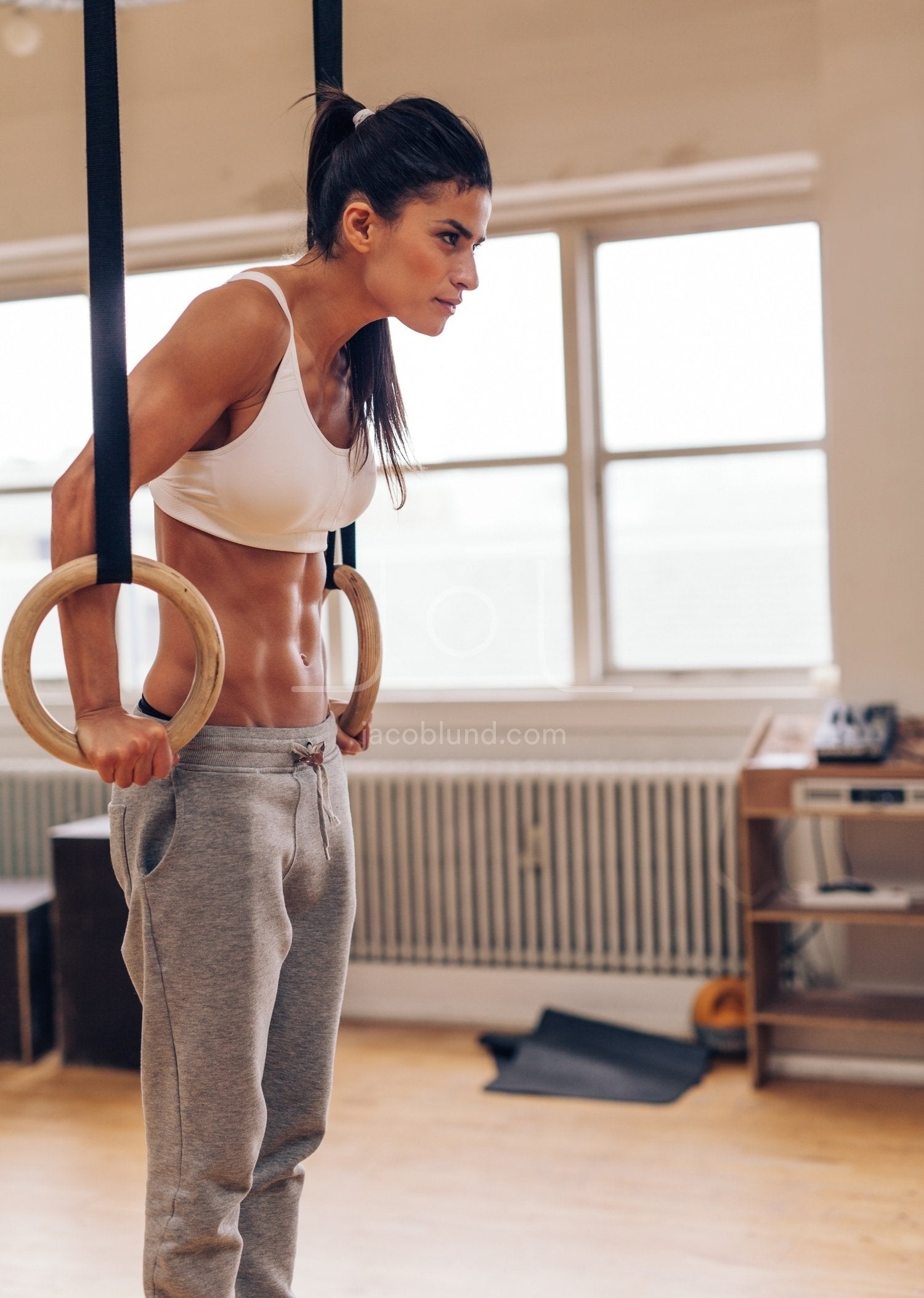 Determined woman exercising with gymnastic rings in gym stock